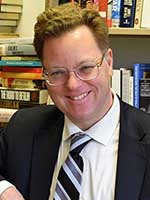 Headshot of a white man with short brown hair wearing glasses and a black suit jacket