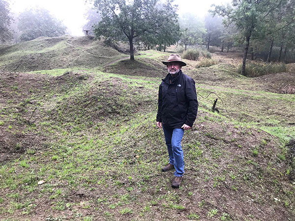 Modern photograph of Todd Harvey standing in a field full of grassy bumps.