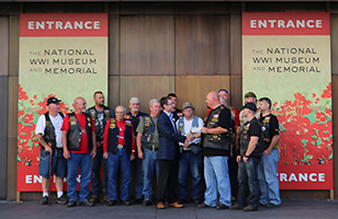 Modern photograph of a group of men wearing leather vests posing in front of the Museum and Memorial's bronze doors.