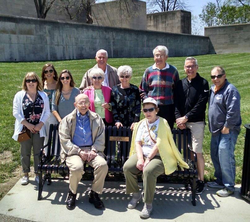 Group of white people of diverse ages gathered around and on a bench on the grounds of the Museum and Memorial.