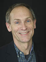 Headshot of a middle-aged white man with greying hair wearing a black suit jacket