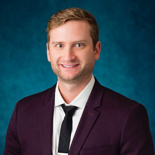 Modern photograph of a young white man with light brown hair wearing a dark purple suit and a black tie.