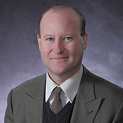 Headshot of a white man with thinning hair wearing a grey suit