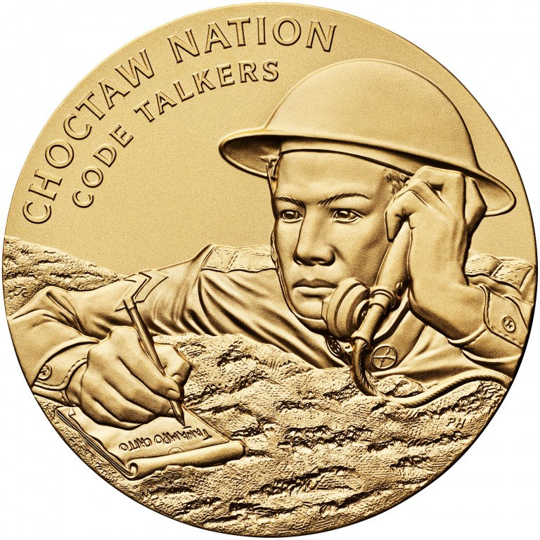 Modern photograph of a bronze-gold-colored medal engraved with an image of a WWI soldier taking notes and communicating over a field radio or telephone. Text: 'Choctaw Nation / Code Talkers'