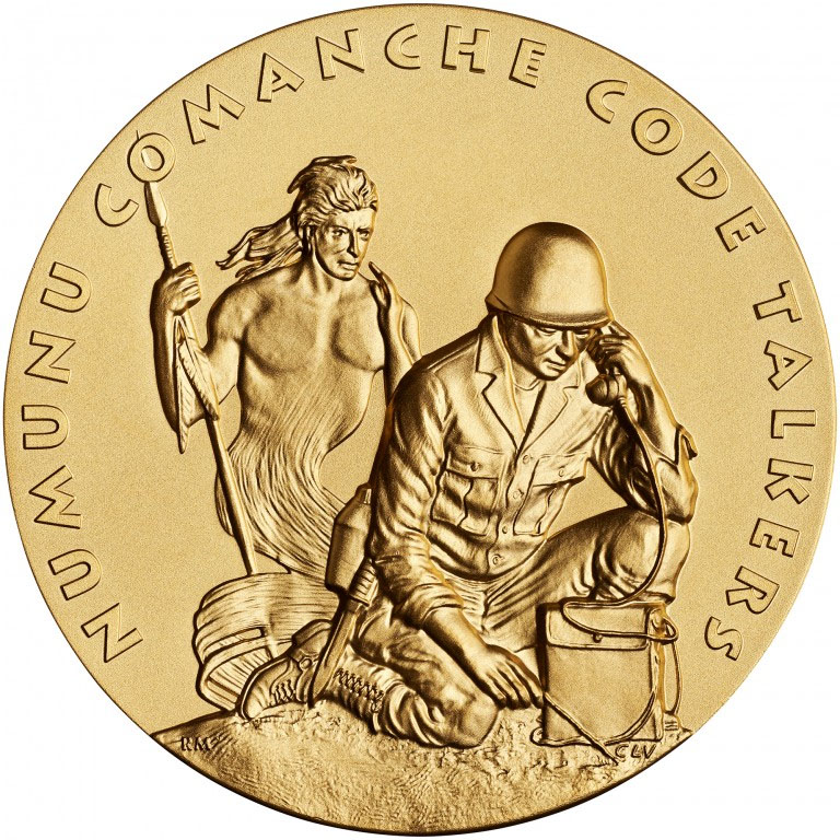 Modern photograph of a bronze-gold-colored medal engraved with a Native American soldier kneeling and speaking into a portable telephone unit while the spirit of a Native American warrior in traditional dress hovers behind him. Text: 'Numunu Comanche Code Talkers'