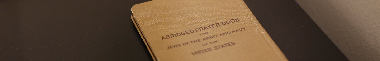 Cropped detail of a small brown book with text printed on the cover: 'Abridged Prayer Book for Jews in the Army and Navy of the United States'