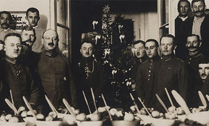 Black and white photograph of a large group of soldiers in uniform posing for the photograph behind a table full of food, in front of a decorated Christmas tree.