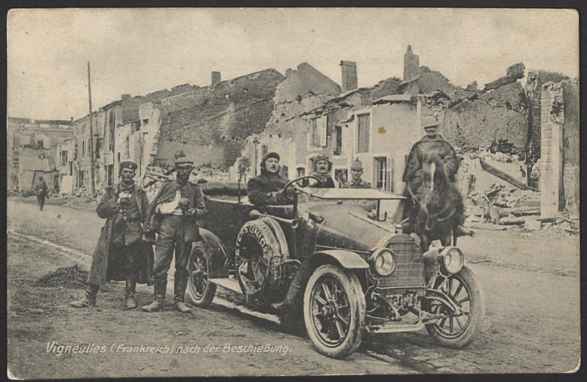 Black and white photo of a group of white European soldiers posed in and around a WWI-era automobile in front of destroyed houses.