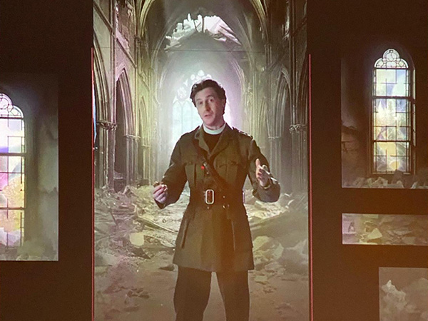 Screenshot of a white male actor in a WWI uniform composited onto a CGI background of a bombed-out cathedral