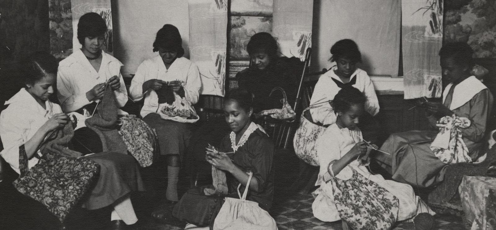 Black and white photograph of a group of Black women gathered in a room knitting various projects