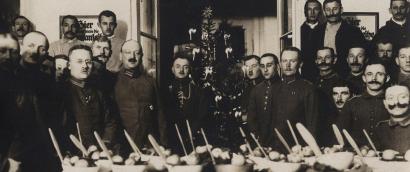 Large group of white men in military uniform gathered around an expansive table filled with food and utensils. There is a Christmas tree in the background.