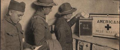 Black and white photograph of three men in military uniform lined up in front of a box labeled 'U.S. Mail'. The one at the front of the line is inserting an envelope into the box.